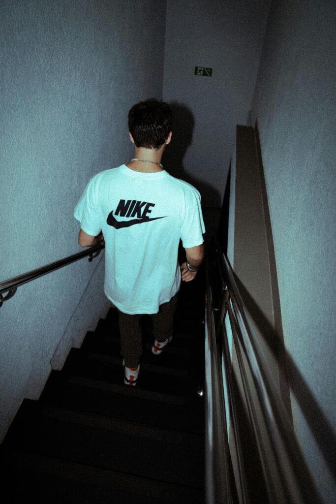 A man in a Nike t-shirt walks down indoor stairs, captured from behind in low light.