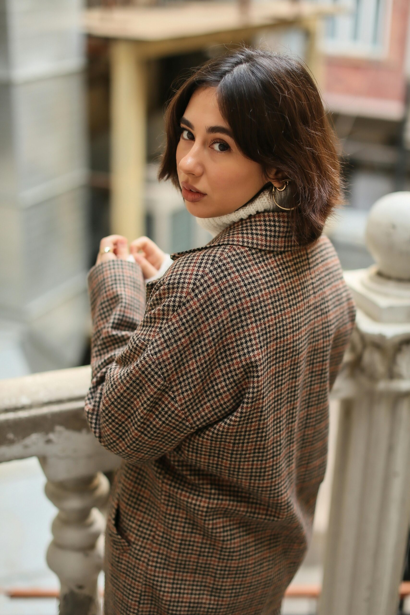 Stylish woman in a checkered blazer gazing back on a vintage staircase.